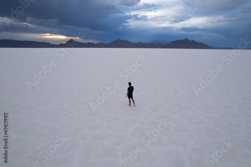 Aerial of man walking in Utah Bonneville Salt Flats with cloudy skies.  Shot on a drone.  Blue cracked salt flat near Salt Lake City  Utah in the western part of the United States.