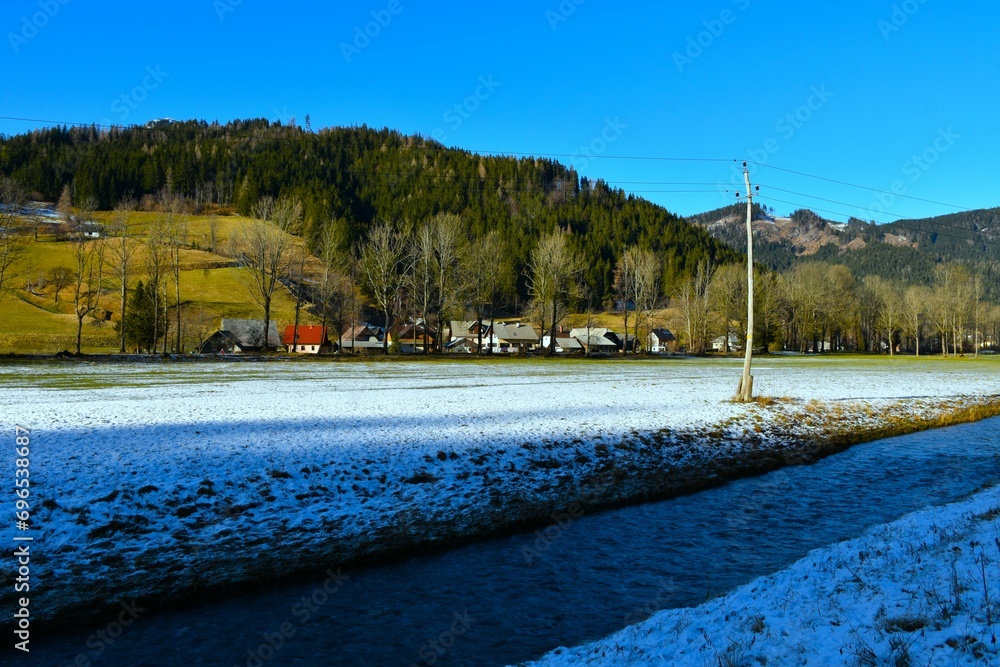 View of Zgornje Jezersko village and Jezernica stream with forest covered hill above in Gorenjska, Slovenia