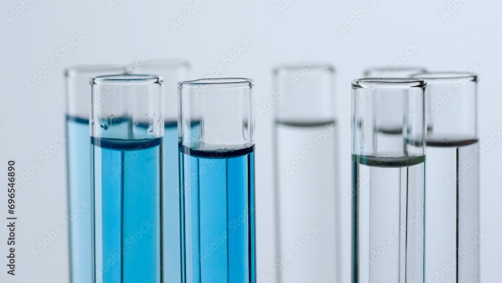 Science and biotechnology creative concept. Close up shot of laboratory glassware on white background. Test tubes with transparent and blue liquid fluid in laboratory, scientific expertise. Science and biotechnology creative concept. Close up shot of laboratory glassware on white background. Test tubes with transparent and blue liquid fluid in laboratory, scientific expertise.