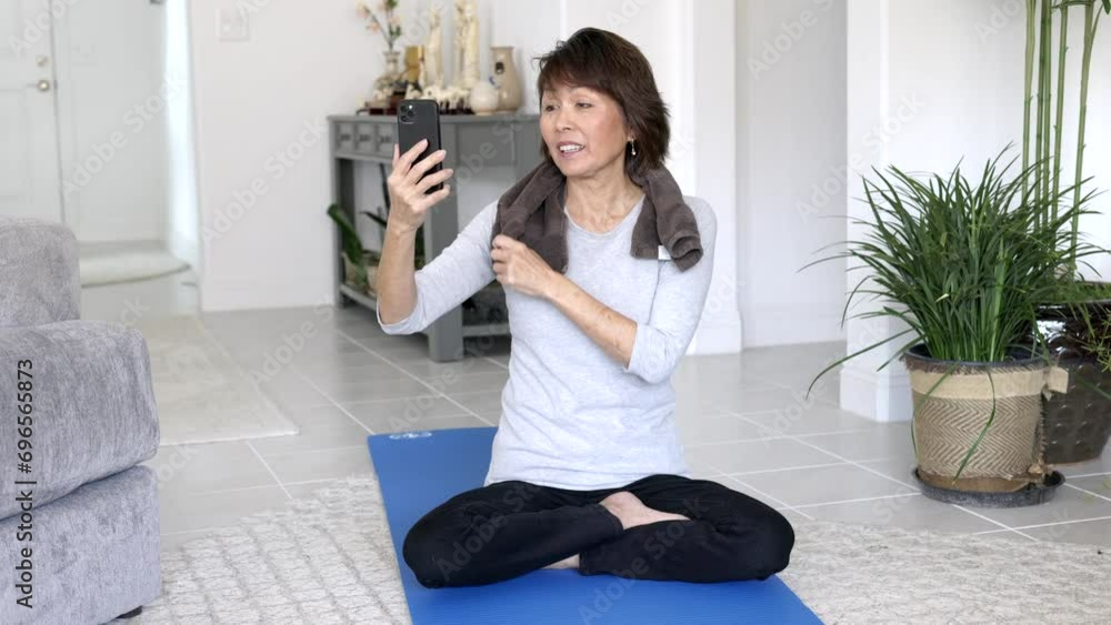 Happy attractive woman smiling video chatting FaceTime laughing holding mobile cell phone sitting on exercise mat Happy attractive woman smiling video chatting FaceTime laughing holding mobile cell phone sitting on exercise mat