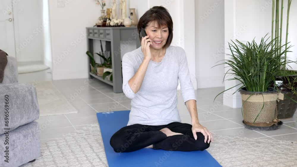 Attractive woman legs crossed smiling talking on mobile cell phone sitting on exercise mat in living room. Attractive woman legs crossed smiling talking on mobile cell phone sitting on exercise mat in living room.