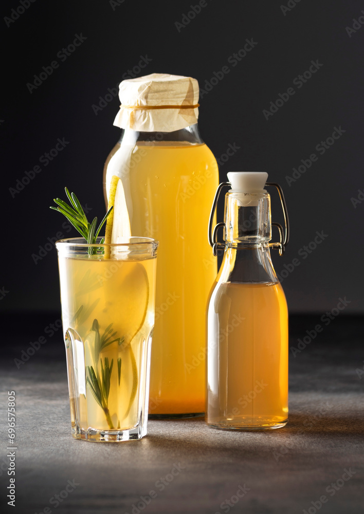 Pear kombucha with rosemary in a glass and bottles on a dark background, vertical orientation, close-up Pear kombucha with rosemary in a glass and bottles on a dark background, vertical orientation, close-up