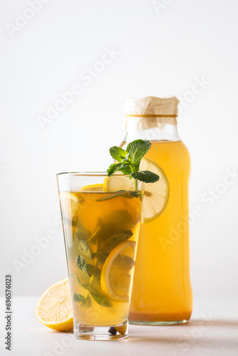 Homemade kombucha with lemon and mint stands in a glass and bottle on a light background, copy space