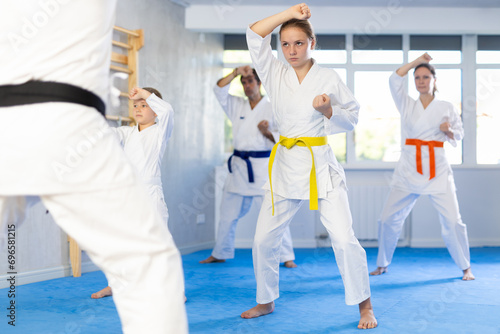 Teen girl and her family during practice of karate kata standing in row and closely watching man teacher, repeat movements and perform exercises. Active and athletic hobby for all family members photo