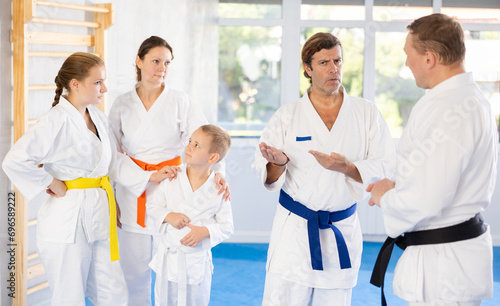 Family in kimono and colored belts discusses and communicates with trainer after martial art training