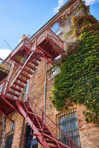 Ivy-Covered Brick Building with Red Fire Escape in Sunlight, Urban Upward View