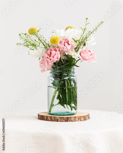 Glass mason jar with fresh wildflowers inside on table photo