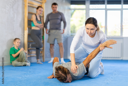 At self-defense training, trainer teaches woman technique of grabbing arm and lowering opponent to floor