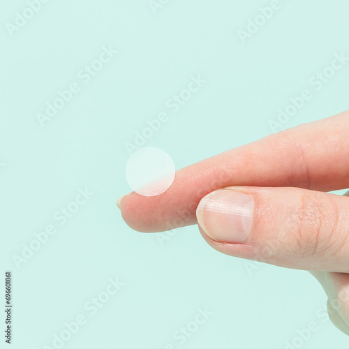 Woman holding pimple patch on green background 
