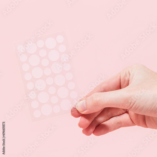 Woman holding pimple patch sheet on pink background 