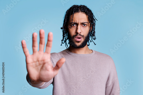 Serious arab man showing stop gesture with arm, looking at camera and talking. Young person making prohibition and rejection sign with confident facial expression portrat photo