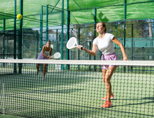 Caucasian woman in t-shirt and shorts playing padel tennis match during training on court.