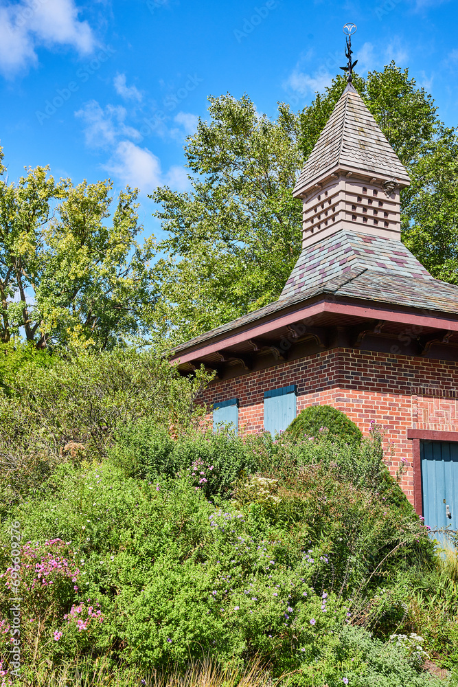 Charming Brick Garden Shed with Weathervane and Lush Foliage Charming Brick Garden Shed with Weathervane and Lush Foliage