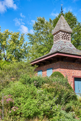 Charming Brick Garden Shed with Weathervane and Lush Foliage