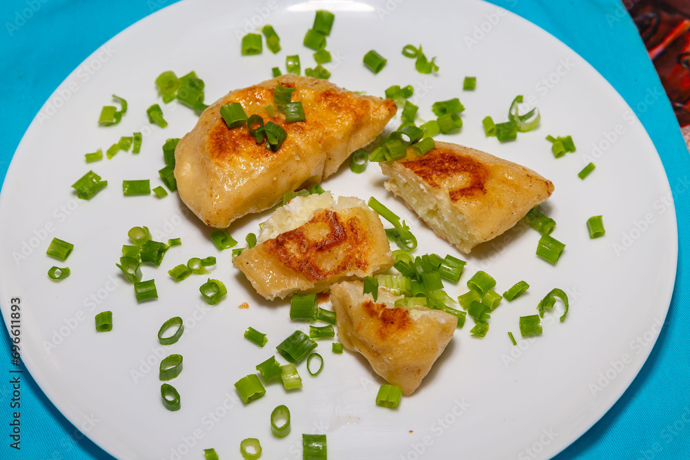 Fried pieroguis Ukrainian traditional food, on white plate on tablecloth decorated with typical Ukrainian embroidery. With cream and fresh chives in fine details. Prudentópolis PR
