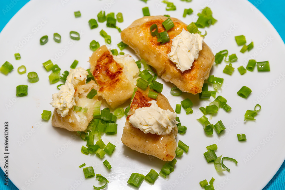 Fried pieroguis Ukrainian traditional food, on white plate on tablecloth decorated with typical Ukrainian embroidery. With cream and fresh chives in fine details. Prudentópolis PR