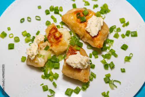 Fried pieroguis Ukrainian traditional food, on white plate on tablecloth decorated with typical Ukrainian embroidery. With cream and fresh chives in fine details. Prudentópolis PR