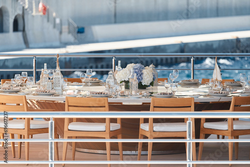 Close-up view of luxurious setting of the banquet table on an expensive mega yacht at sunny day, with awnings stretched over the deck to protect from the sun, wealth life, flowers and chairs photo