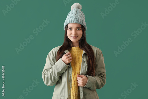 Young woman in warm hat and jacket on green background