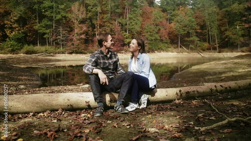 Couple Sit and Talk on Log next to Mountain Lake