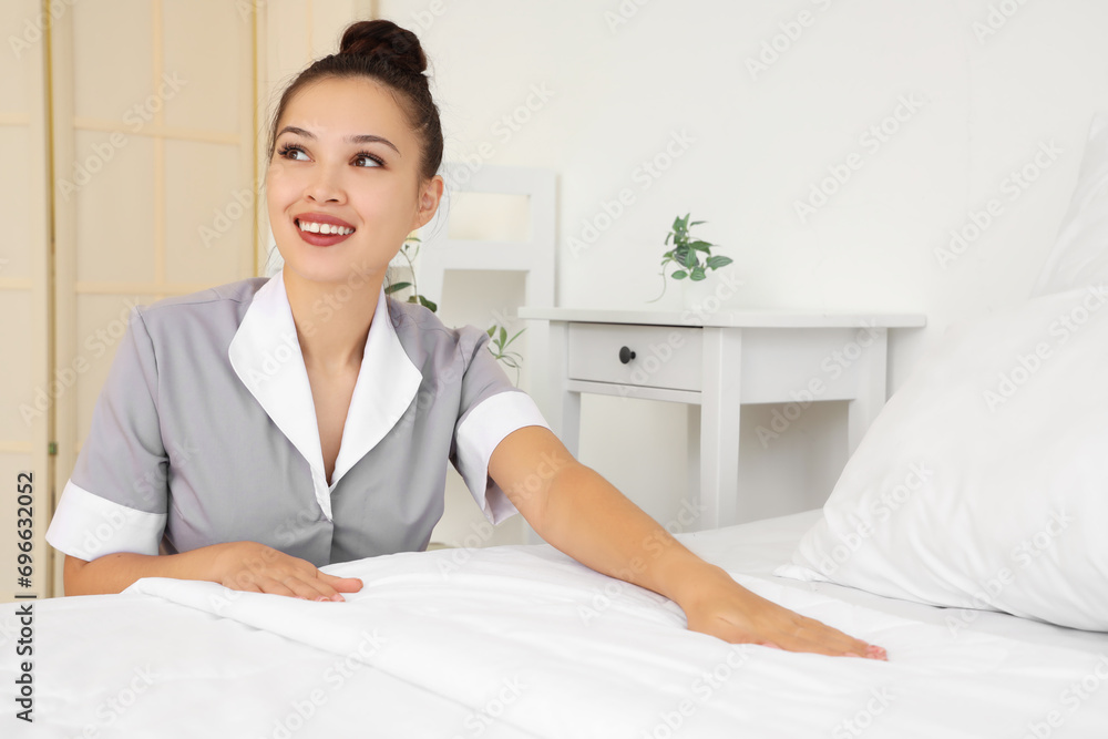 Pretty chambermaid making bed in light hotel room Pretty chambermaid making bed in light hotel room