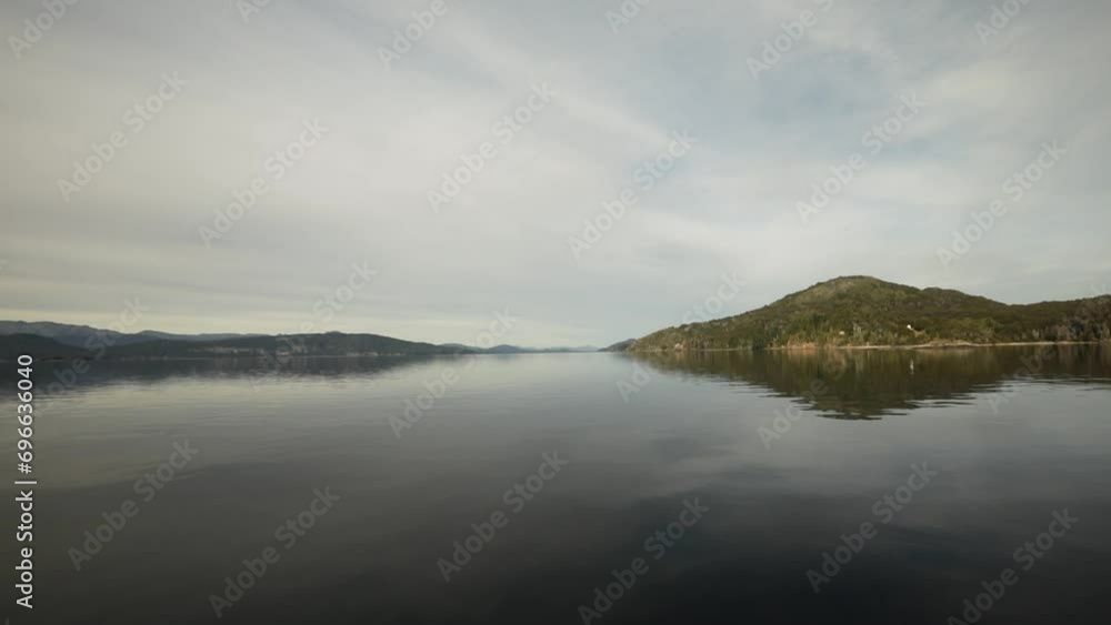 A boat sailing the lake. The forest and rocky mountains in the surroundings. Beautiful sky and landscape reflection in the water surface. 
