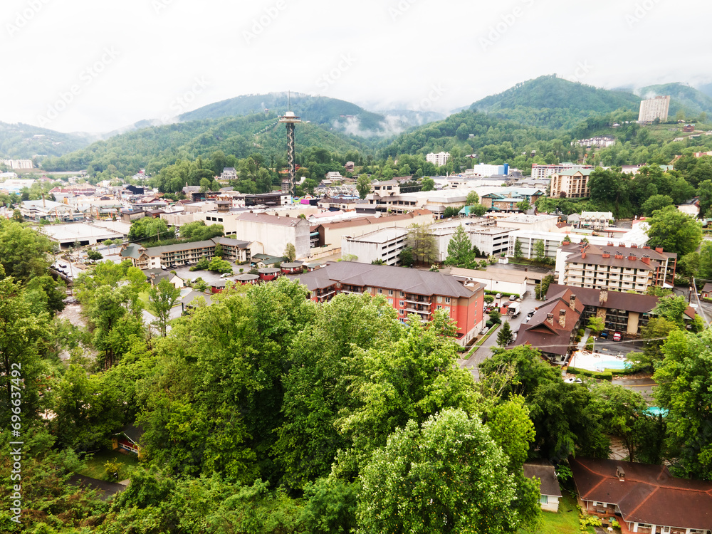city of Gatlinburg in Tennessee and the Great Smoky Mountains from a bird's eye view. Clouds hang over the forest in the mountains.