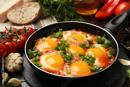 Delicious shakshuka in frying pan and products on wooden table, closeup