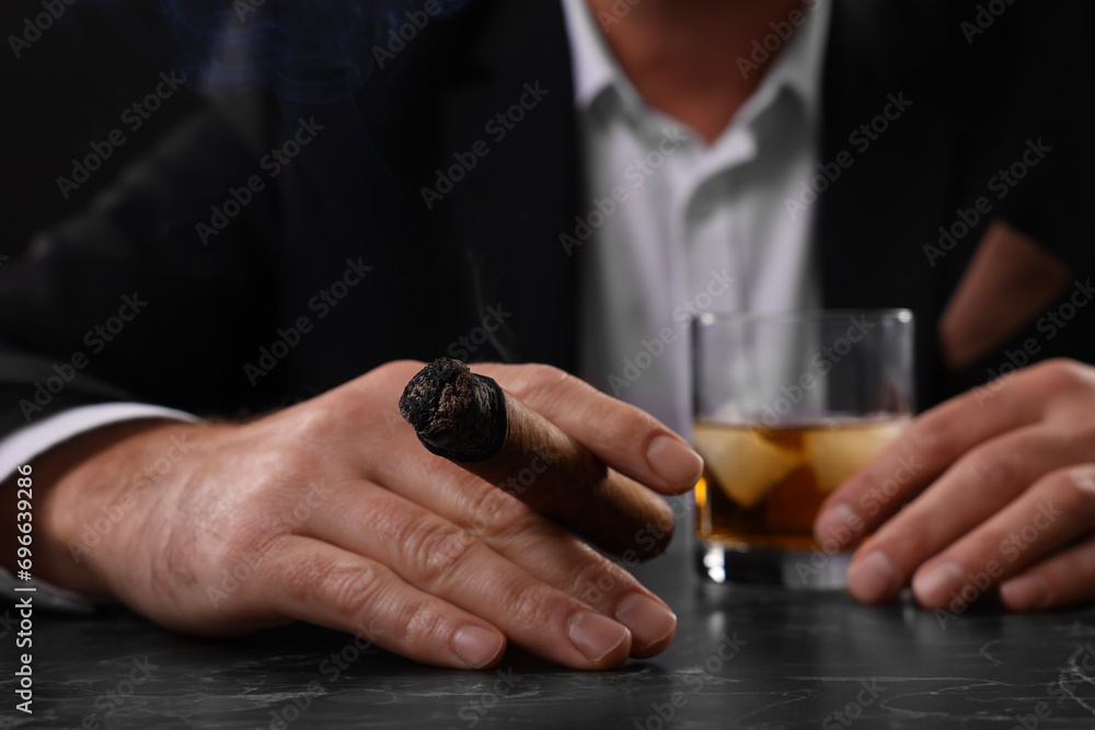 Man with glass of whiskey smoking cigar at dark marble table, closeup Man with glass of whiskey smoking cigar at dark marble table, closeup