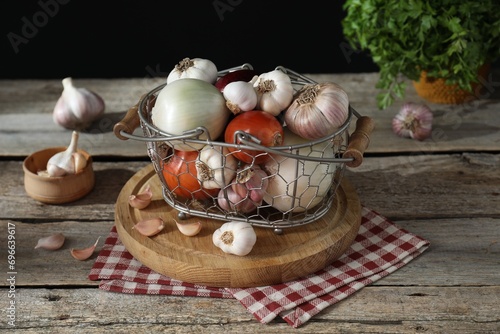 Fresh raw garlic and onions in metal basket on wooden table