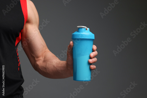Young man with muscular body holding shaker of protein on grey background, closeup. Space for text photo