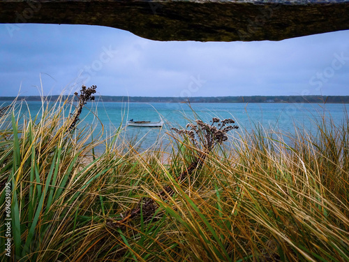 Oak Bluffs Martha’s Vineyard Seascape with seagrass on sand dune and a fishing boat on Sengekontacket Pond along Joseph Sylvia State Beach in Massachusetts, USA