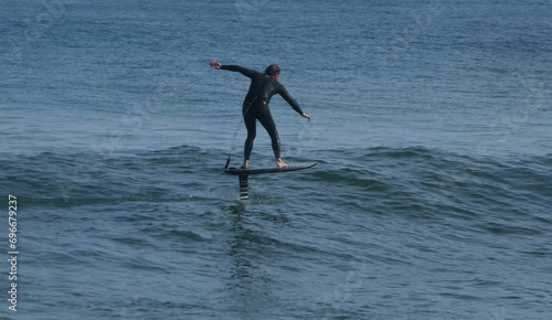 Photos rear view of man wearing wetsuit surfing on hydrofoil board