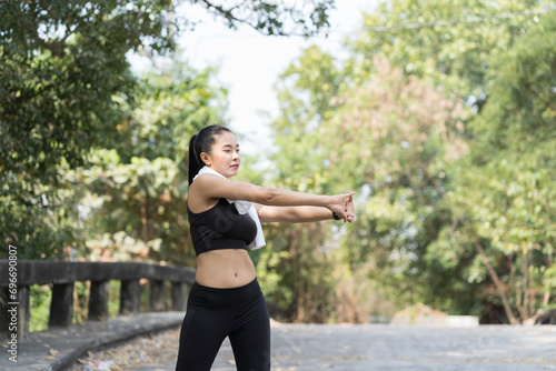 Smiling asian woman wearing black sportswear and sweat wipes on neck and exercising outdoor. Healthy and sport concept