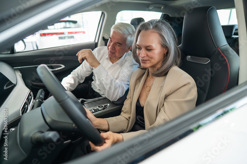 An elderly couple chooses a new car at a car dealership. Mature woman driving. 