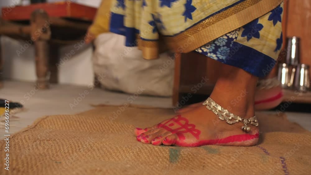 A closeup shot of a woman wiping her bare feet on a rucksack doormat - cleanliness and hygiene  house rules. A rural household in an Indian village - a poor family  a single lady  BPL  wearing paya...