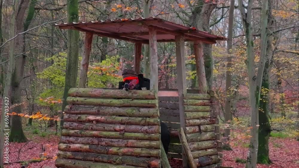 Slow motion shot of a hunter sitting on a high stand and aiming at the camera. The camera flies slowly towards him. Slow motion shot of a hunter sitting on a high stand and aiming at the camera. The camera flies slowly towards him.