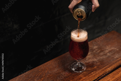 Hand pouring cold black beer from mockup can to wine glass. Summer refreshing drink.