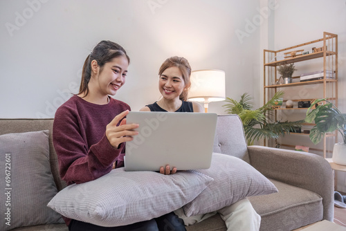 Two women communicate with friends and classmates via video link using laptop and smartphone in living room. Friends, friendship, time together.