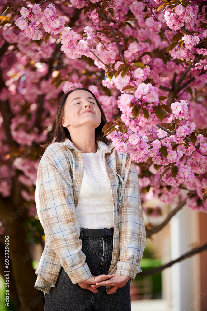 Woman allergic enjoying after treatment from seasonal allergy. Portrait of happy beautiful woman smiling with eyes closed in front of blooming sakura tree at springtime. Spring allergy concept. Woman allergic enjoying after treatment from seasonal allergy. Portrait of happy beautiful woman smiling with eyes closed in front of blooming sakura tree at springtime. Spring allergy concept.