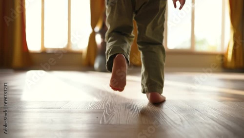Baby takes first step on floor to his mother with bare feet.Son and mother at home feet on floor.Happy boy barefoot on laminate.Baby foot on wooden floor.Child is learning to walk.Happy family concept photo