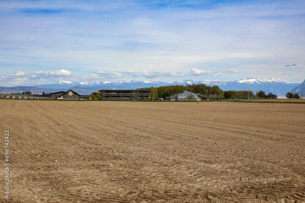 Vue des écoles d'Etoy depuis les champs labourés avec les Alpes en arrière plan