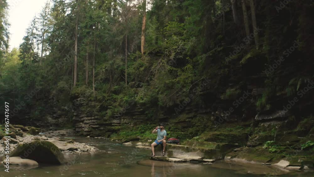 A lonely traveler rests on a stone by the river. Footage from a drone 4k A lonely traveler rests on a stone by the river. Footage from a drone 4k