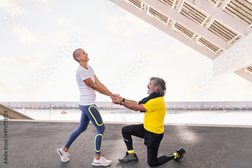 female personal trainer helps a senior sports man get up while they laugh happy after training, concept of active and healthy lifestyle