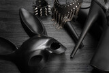 Black rabbit mask, studded leather bracelets, high heels shoes and neck choker on the black wooden table background close up.