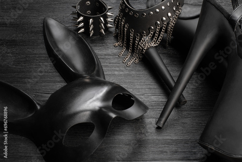 Black rabbit mask, studded leather bracelets, high heels shoes and neck choker on the black wooden table background close up. photo
