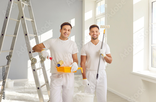 Fotografía Portrait of smiling happy team of house painters looking at camera holding paint rollers and going to paint the wall of new apartment