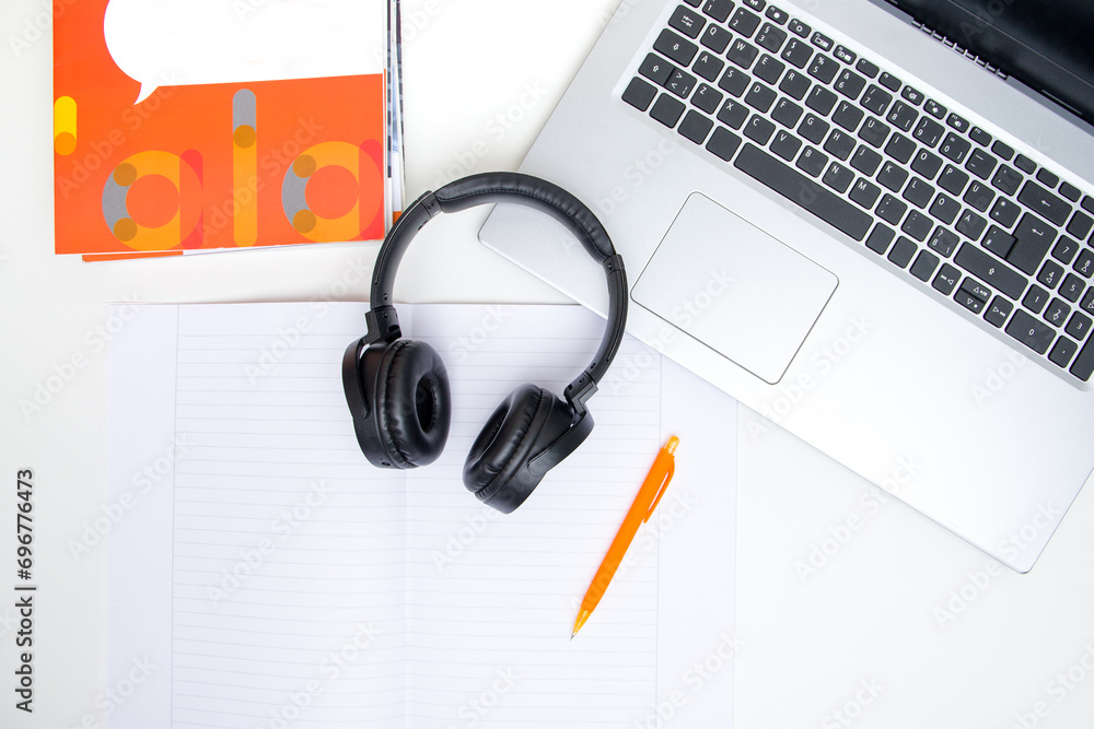 Top view of a laptop, headphones and a notebook on white background