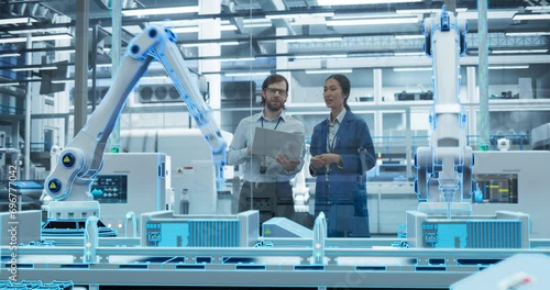Electronics Factory Digitalization: Automated Robot Arm Assembly Line Manufacturing Advanced Equipment. Managers Discussing Work while Futuristic AI Computer Vision Analyzing, Scanning Production Line photo