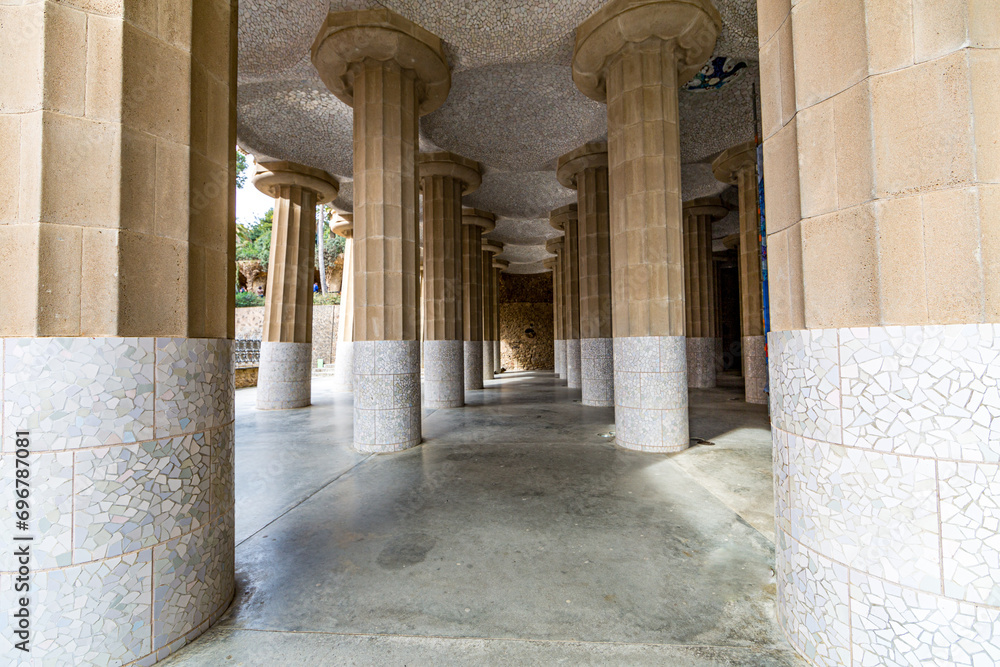 Fototapeta premium Front perspective of hall with columns with fragments of tiles and ceiling with small domes, Hypostyle room in Park Güell by Antoni Gaudí, sightseeing day in Barcelona, Catalonia Spain